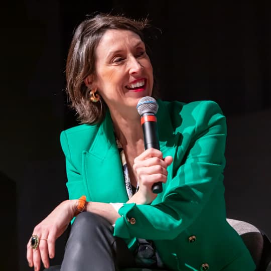 A woman MC at a women's conference wearing a teal jacket.